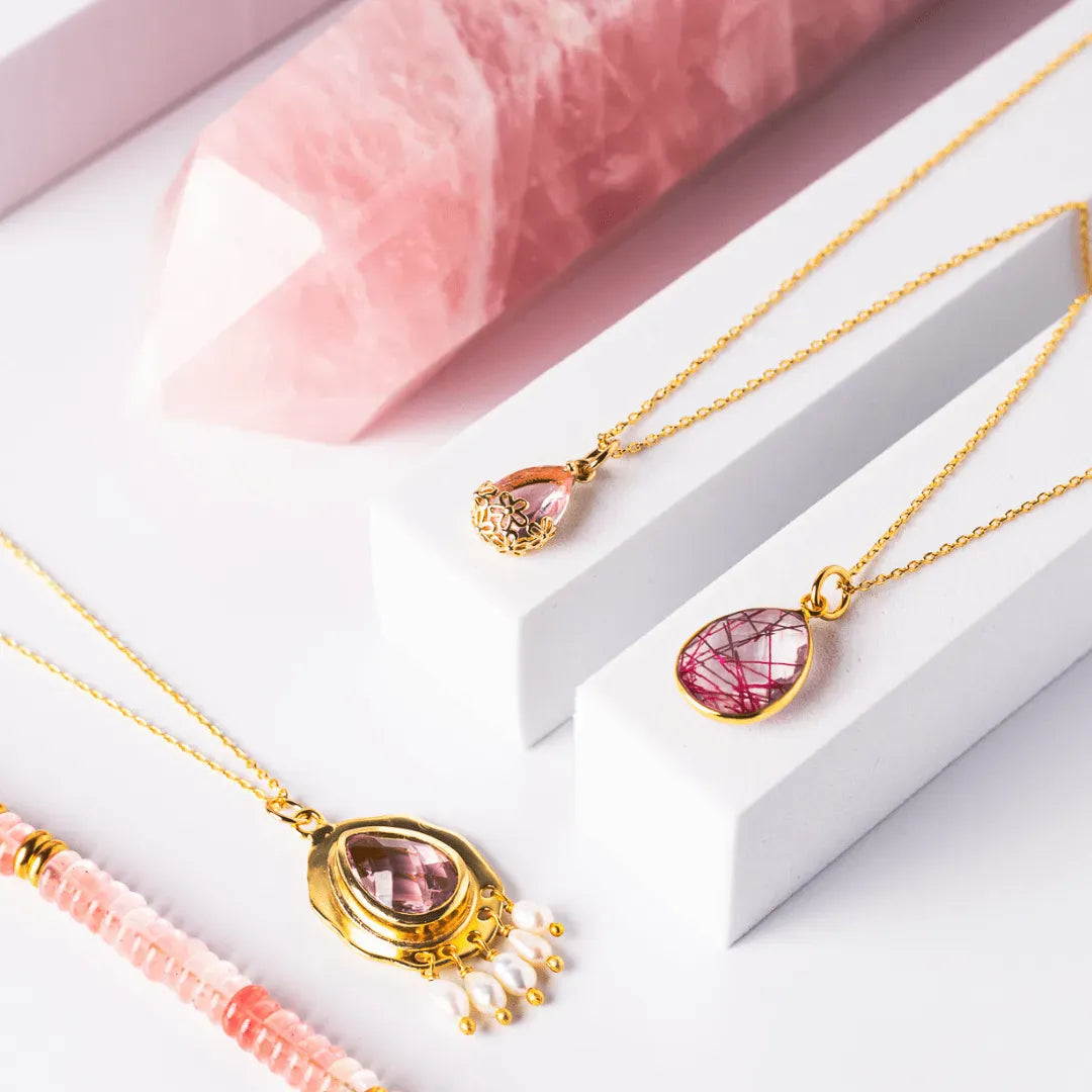 Gold necklaces with pink gemstones on a white stand with a pink background
