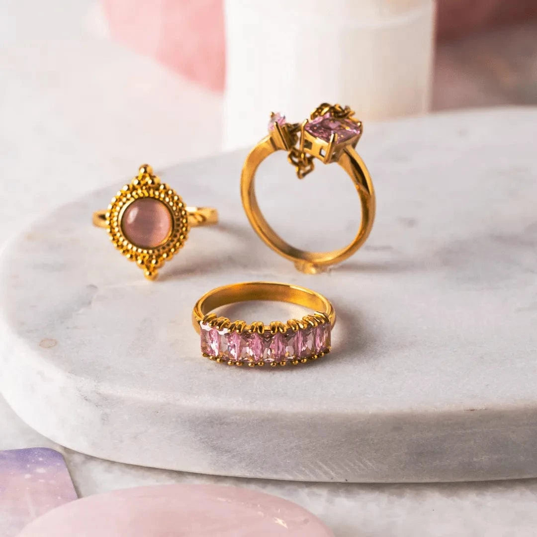 Three gold rings with pink gemstones on a marble surface