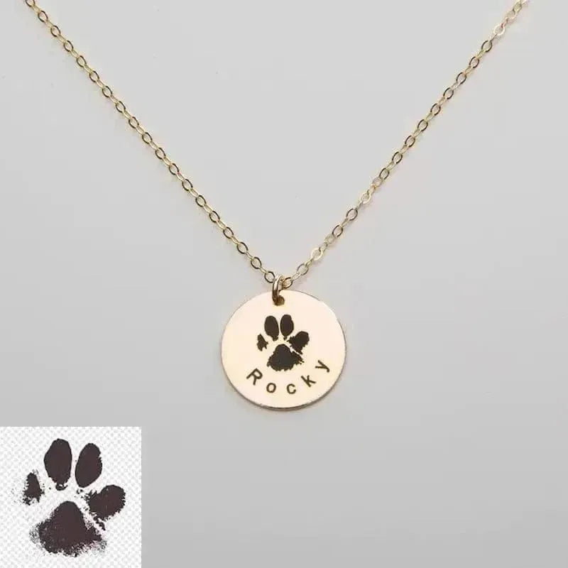 Gold necklace with paw print pendant and 'Rocky' engraving on a gray background