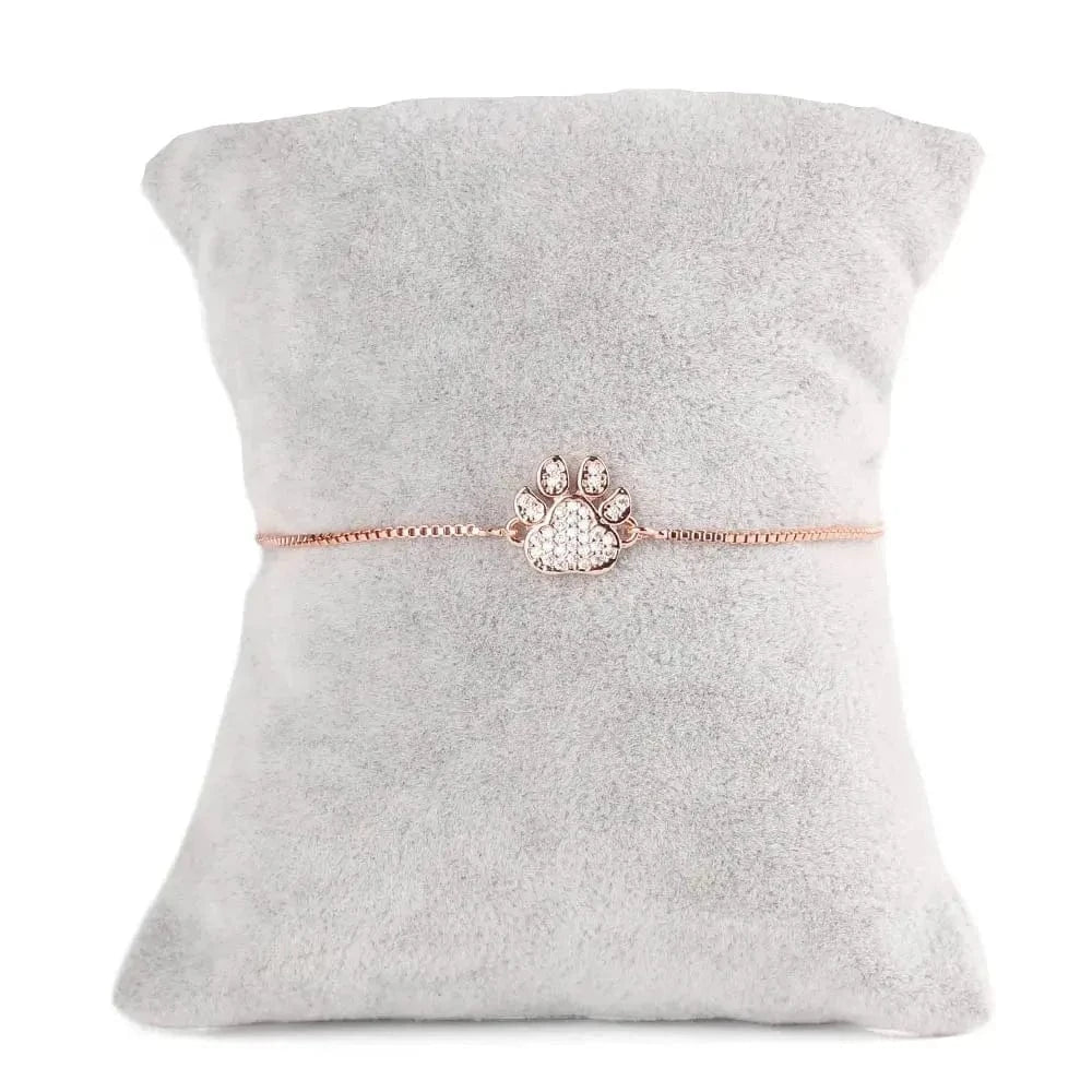 Rose gold paw print bracelet on a gray pillow
