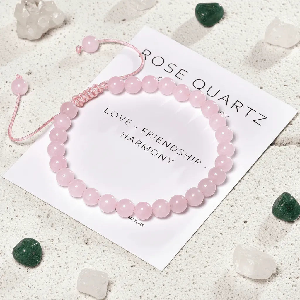 Pink rose quartz bracelet on a card with 'Rose Quartz' text, surrounded by crystals on a light surface.