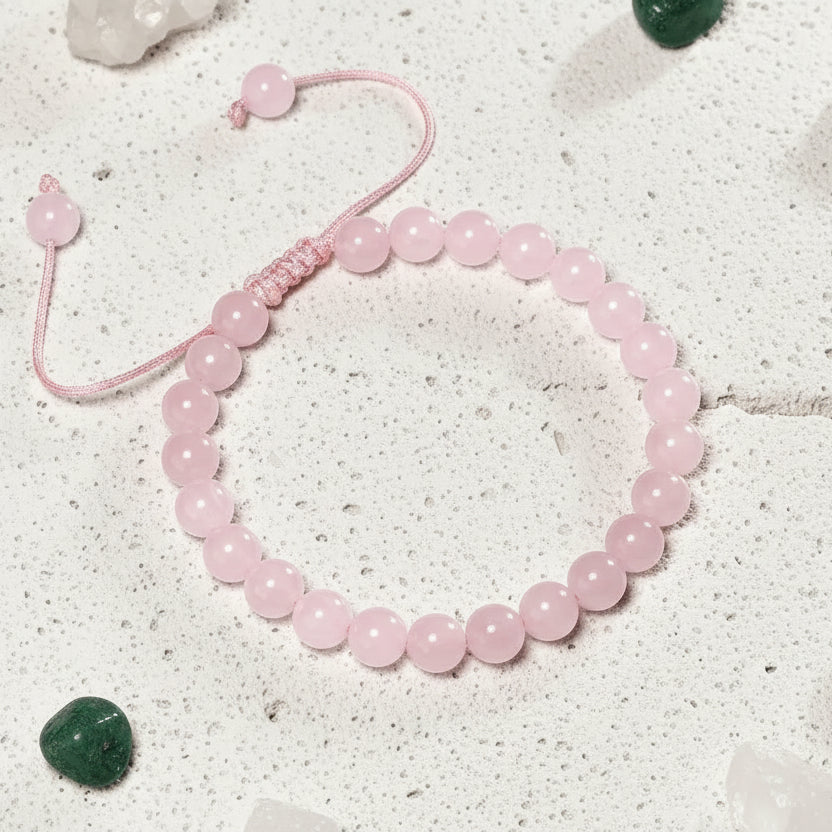 Pink rose quartz bracelet on a card with 'Rose Quartz' text, surrounded by crystals on a light surface.