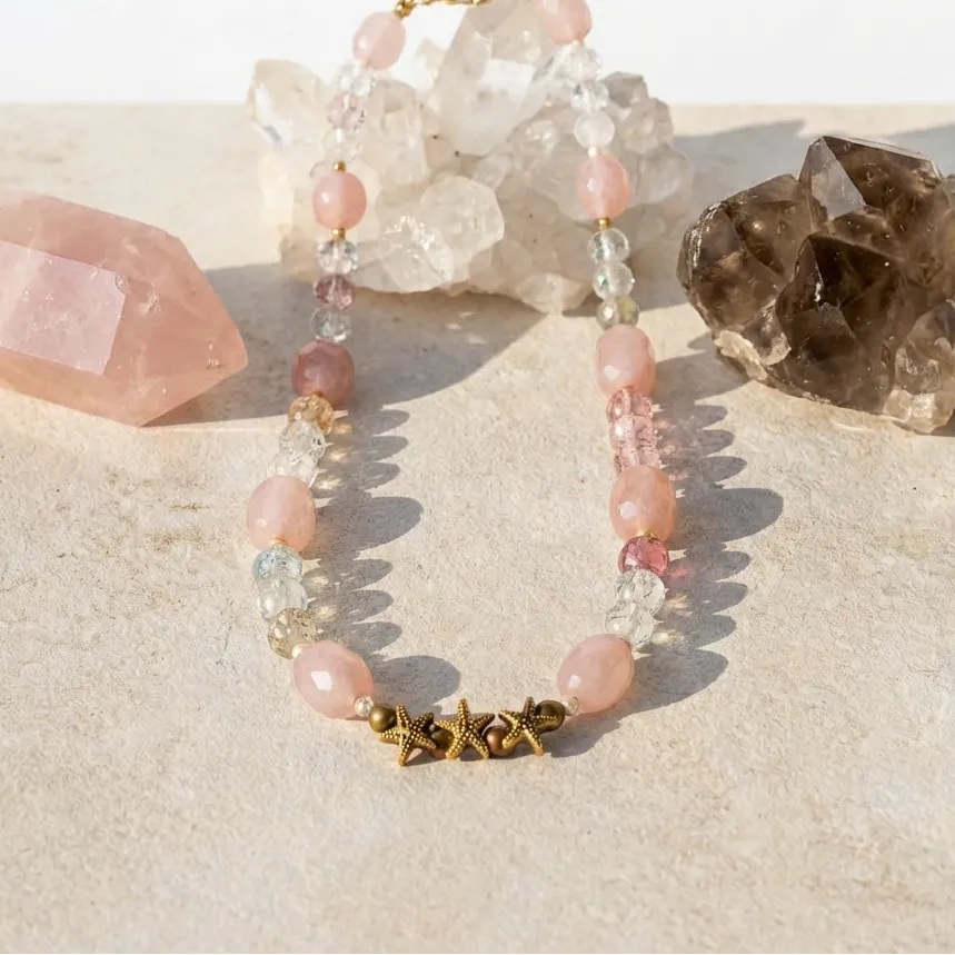 Bracelet with pink beads and gold accents on a sandy surface with crystals.