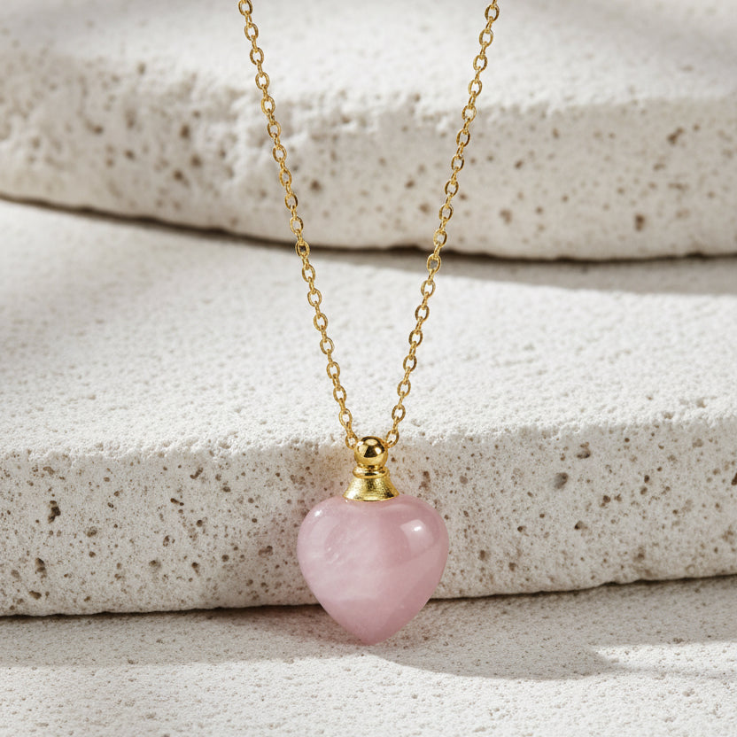 Necklace with a pink heart-shaped pendant on a gold chain against a black background.