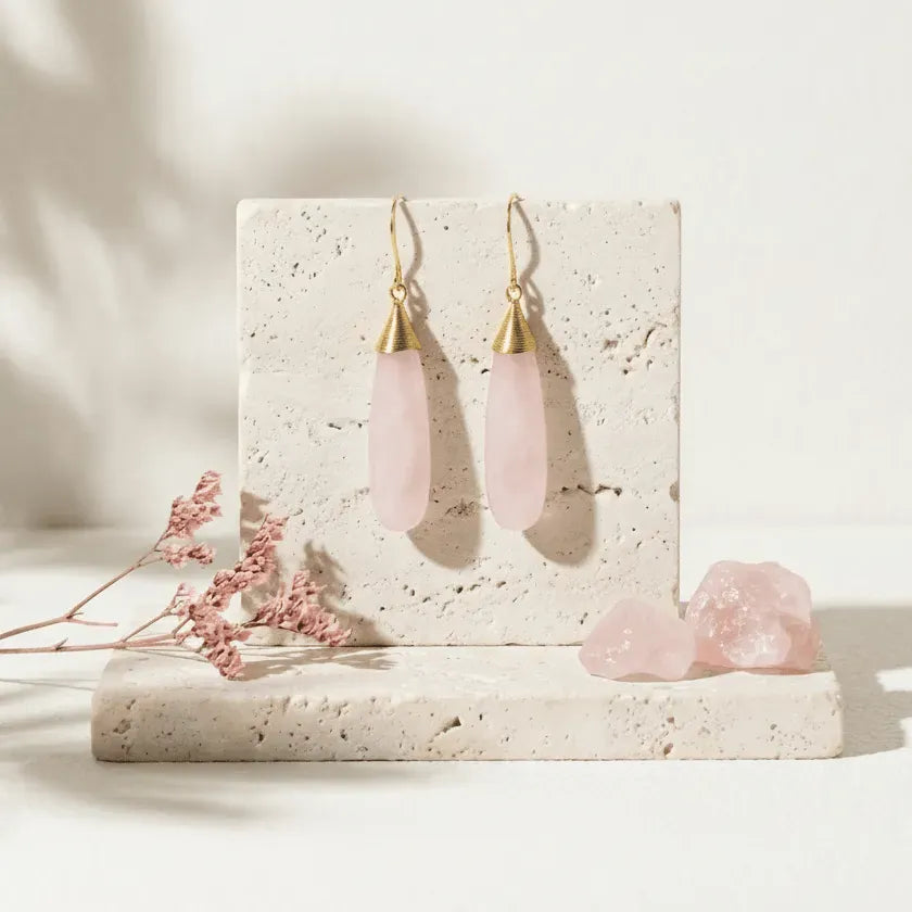 Pink teardrop earrings with gold hooks on a stone surface with pink flowers.