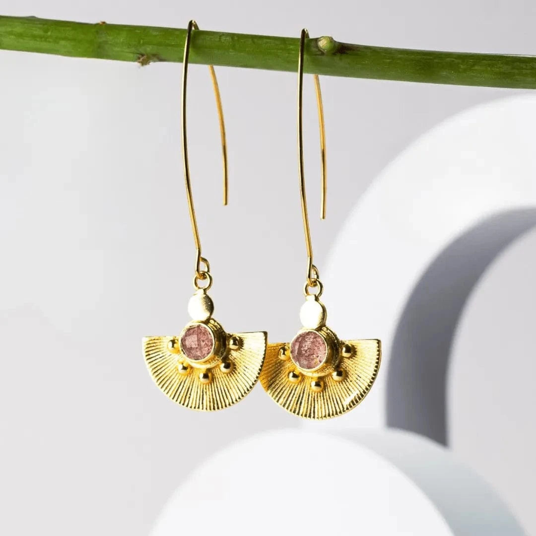 Gold earrings with pink stones hanging from a branch on a white background