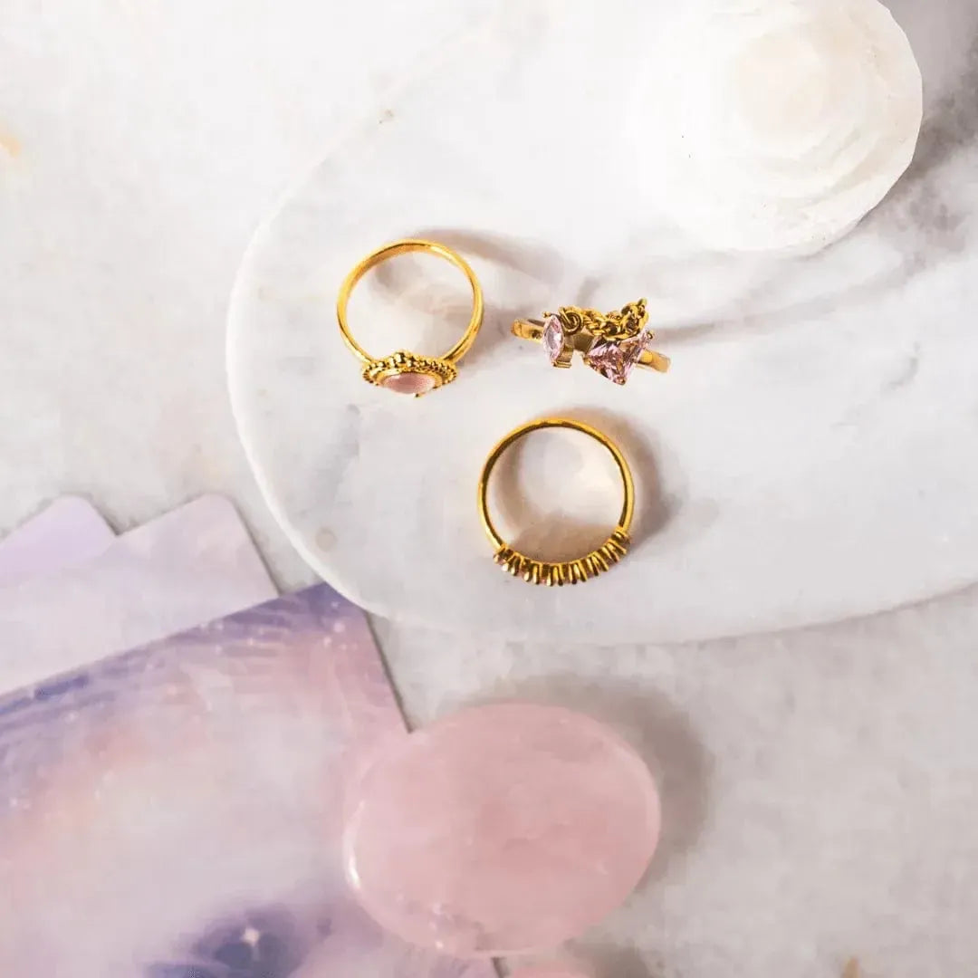 Three gold rings on a white marble surface with pink stones.