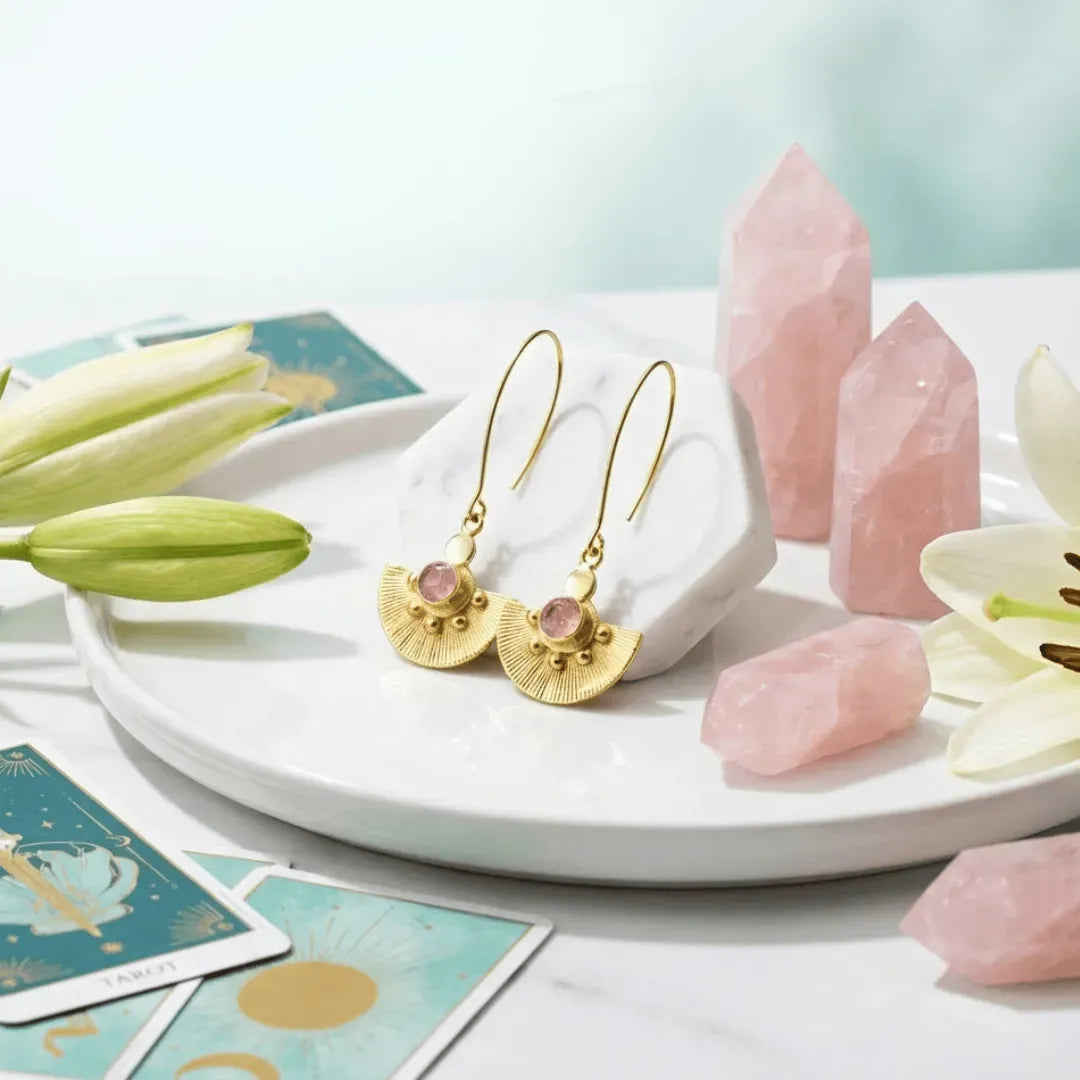 Gold earrings with pink stones on a white dish with crystals and flowers