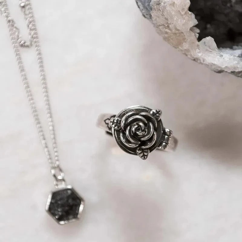 Silver rose-shaped pendant on a chain with a hexagonal black stone, placed on a white surface.