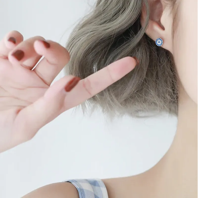 Person wearing a blue evil eye stud earring with a white background