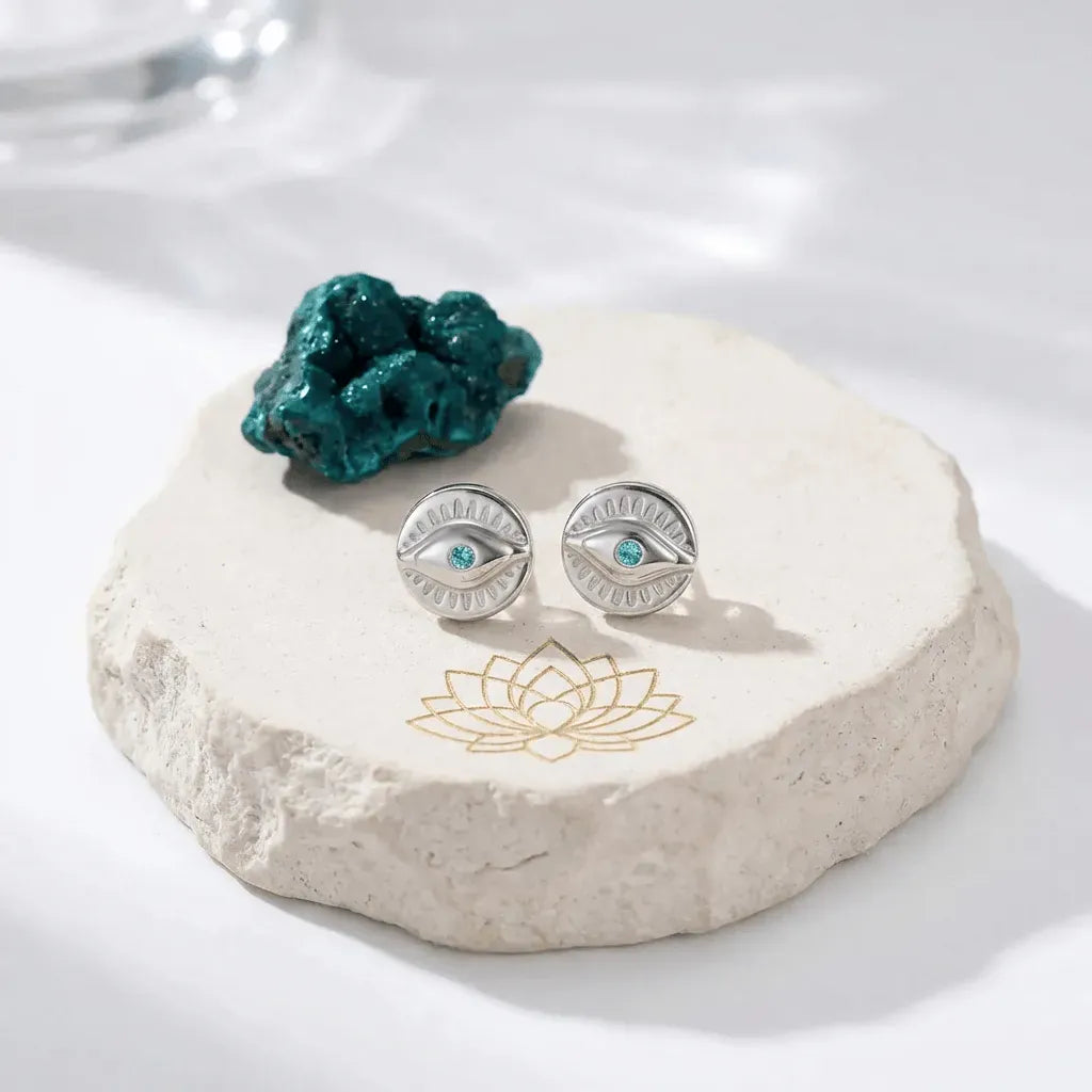 Silver eye-shaped earrings with blue gemstones on a white stone surface with a lotus design.