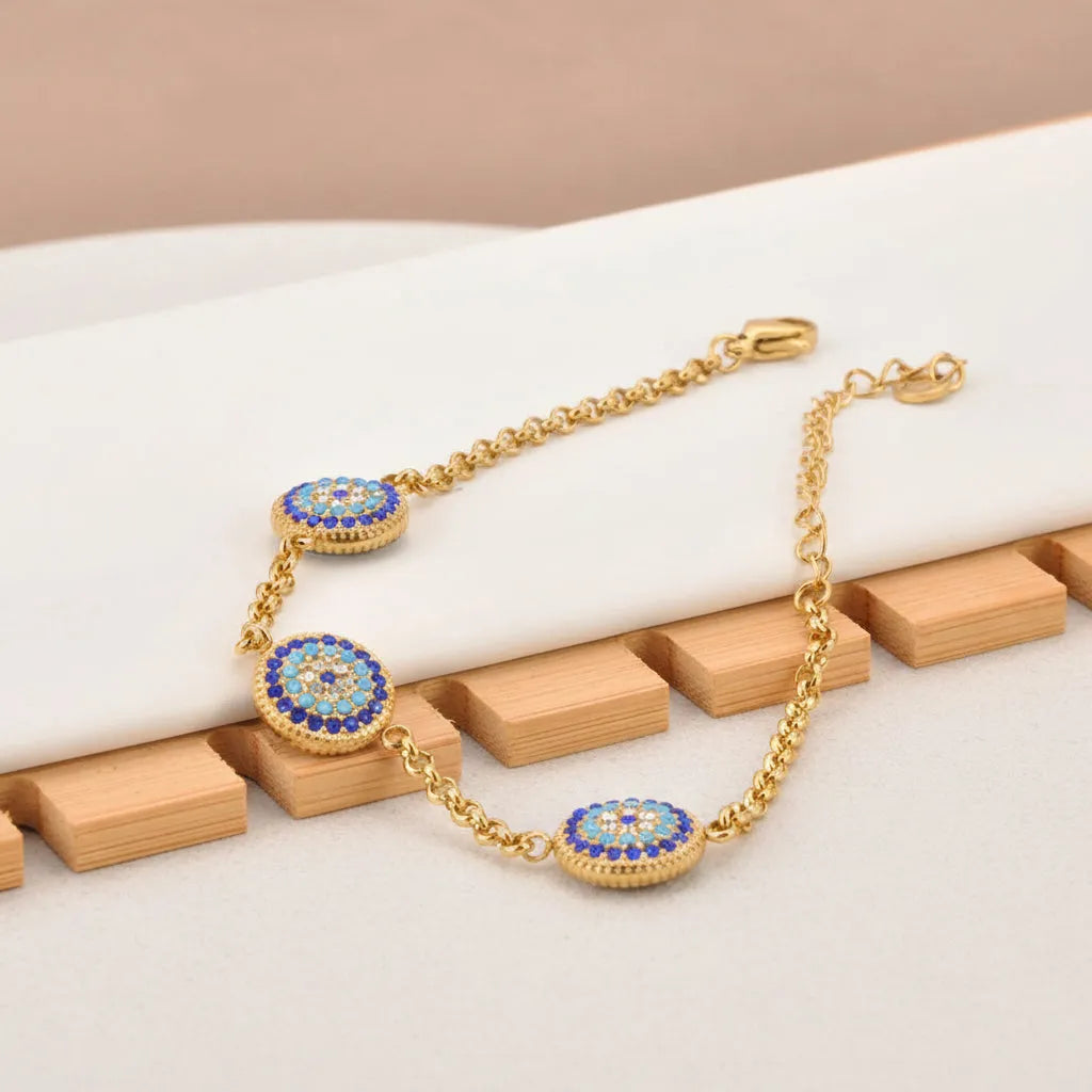 Gold bracelet with blue and red gemstones on a beige surface with berries and leaves.