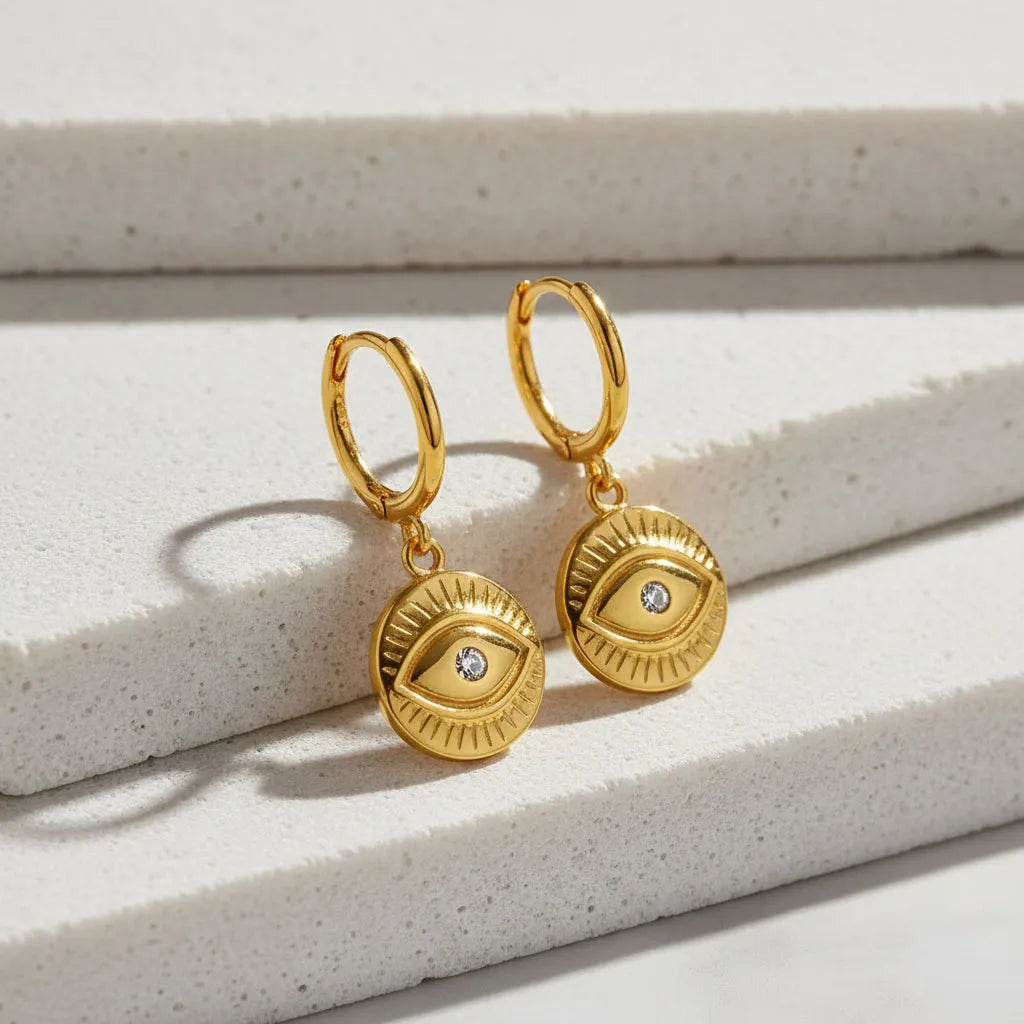 Gold earrings with eye design on a white background