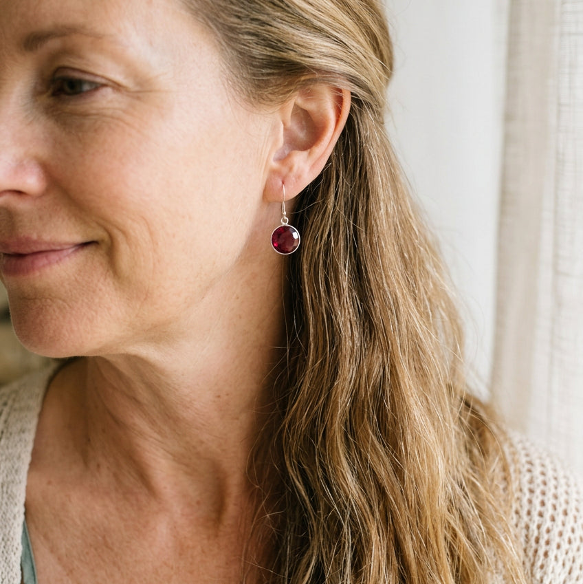 Woman wearing silver drop earrings with round ruby red hydro quartz stones, July birthstone alternative