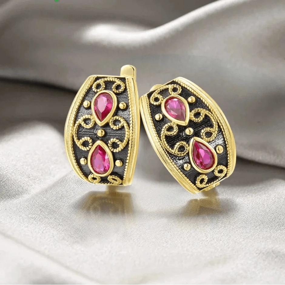 Gold and black earrings with pink gemstones on a satin background