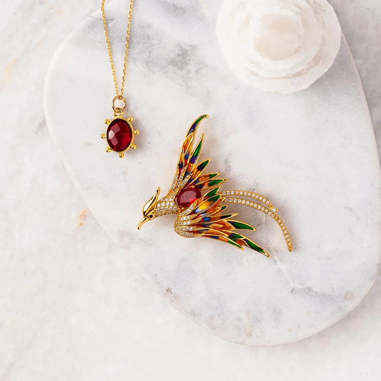 Gold bird-shaped brooch with colorful enamel details on a marble surface