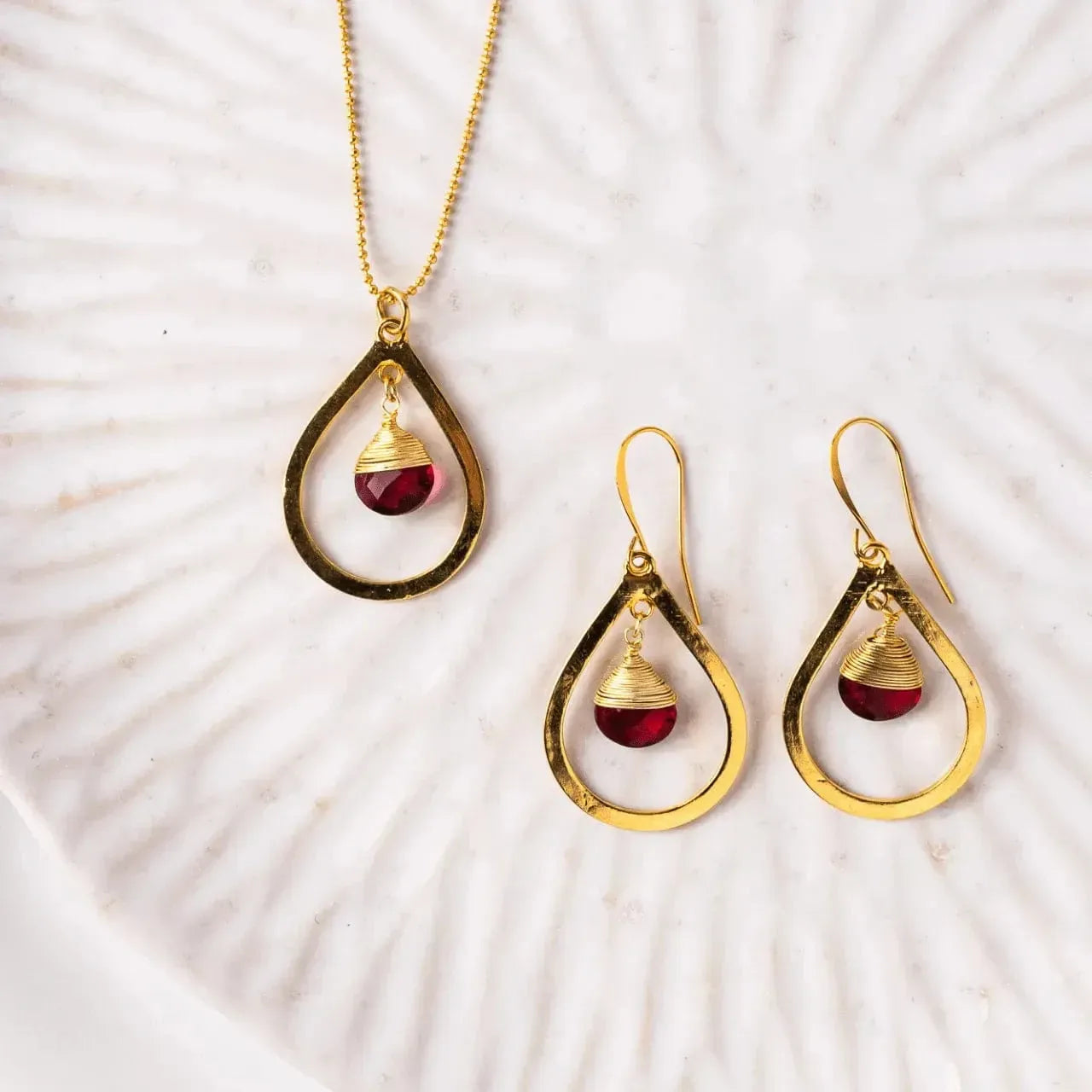 Gold jewelry set with red gemstones on a shell background