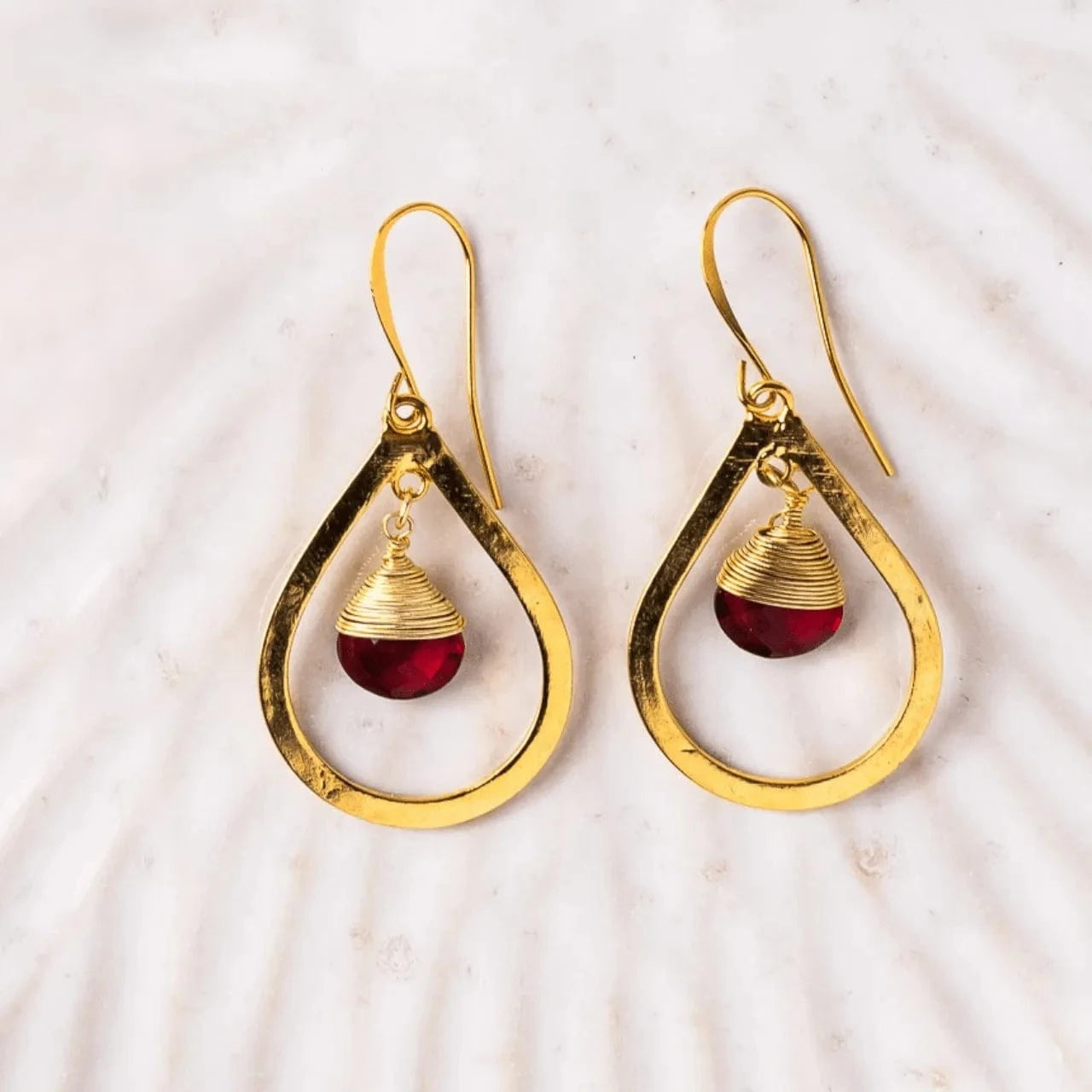 Gold earrings with red gemstones on a marble surface