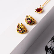 Gold rings with red gemstones and a matching necklace on a white surface.