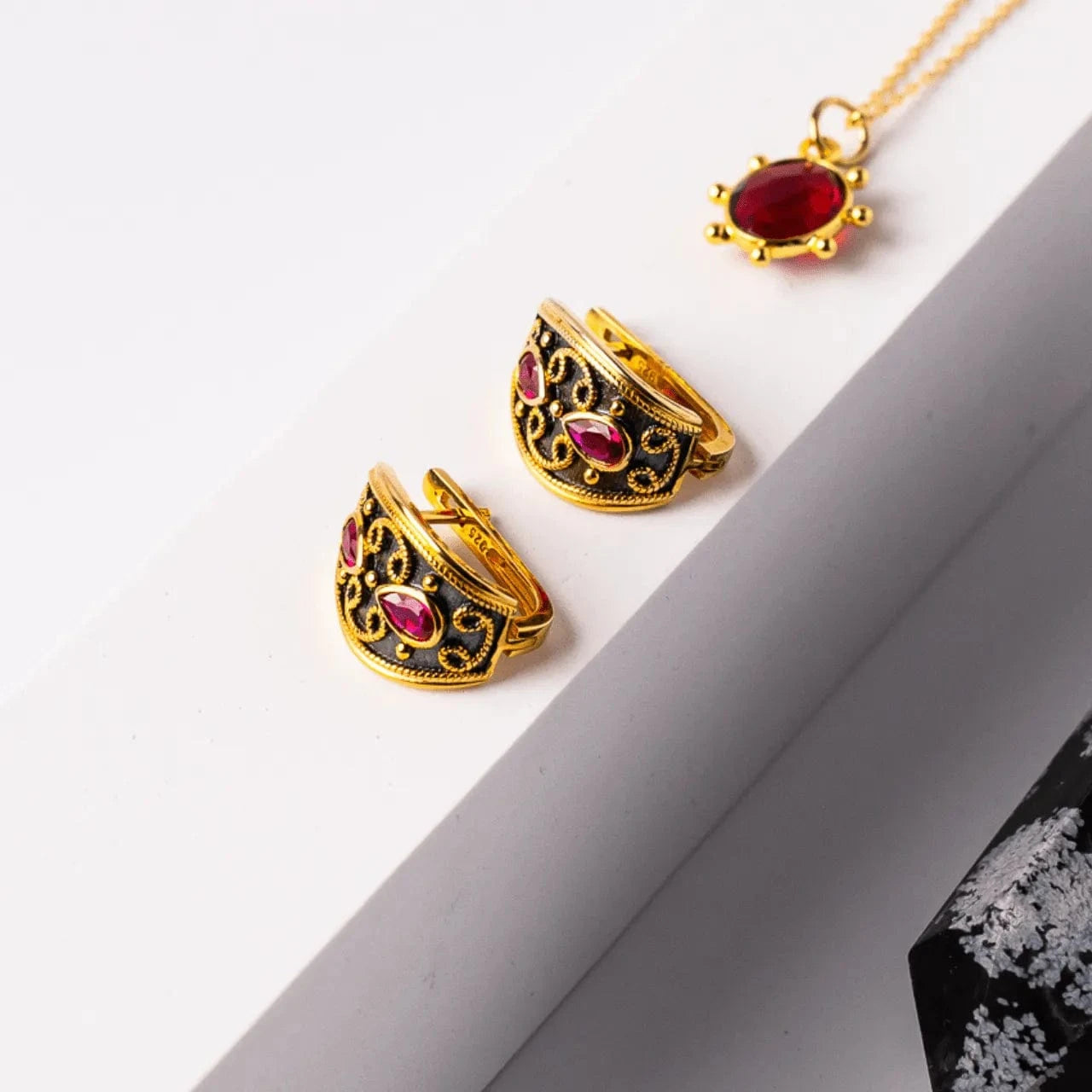 Gold rings with red gemstones and a matching necklace on a white surface.