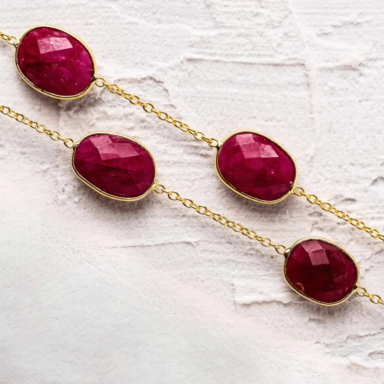 Gold necklace with red gemstones on a textured white background