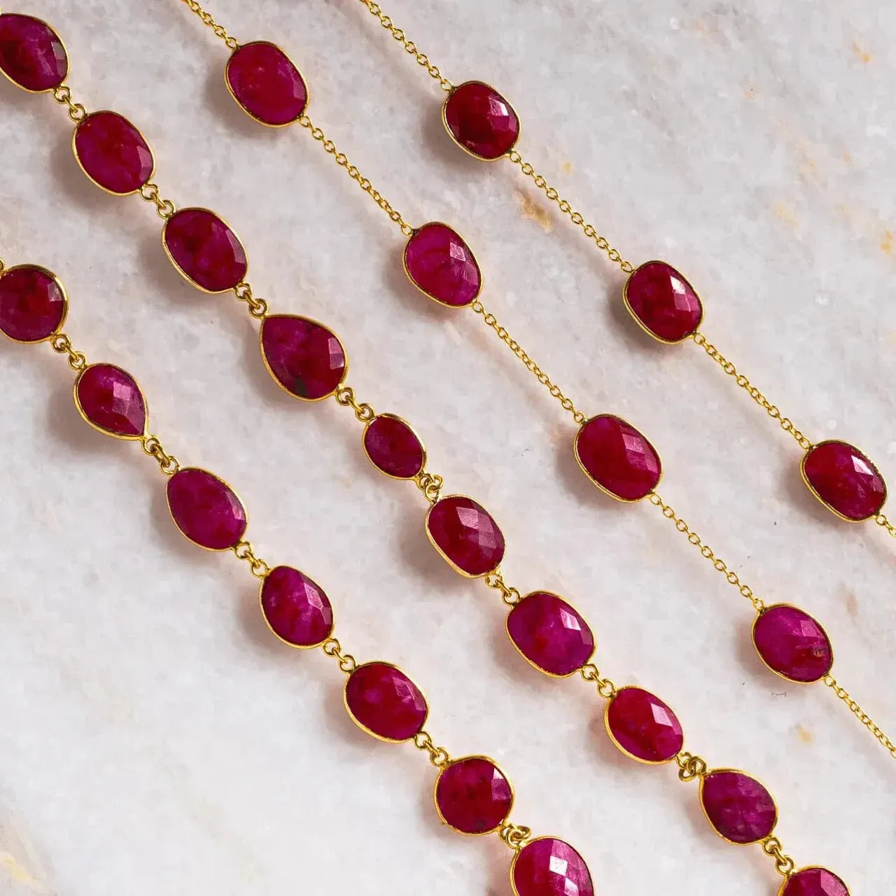 Gold chain necklace with red gemstones on a light background