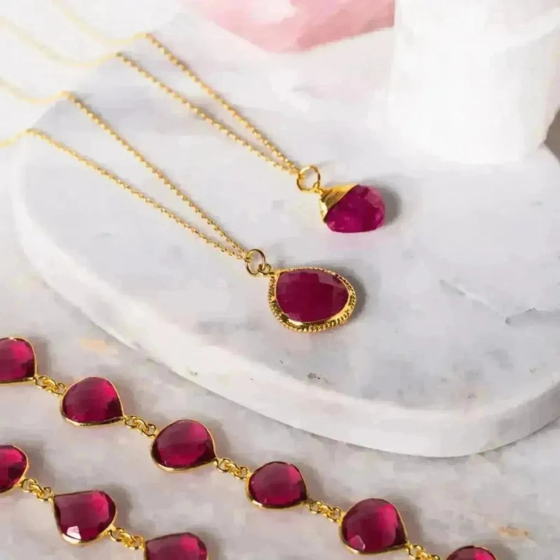 A gold-plated sterling silver necklace with a faceted opaque ruby gemstone pendant, displayed on a white marble surface.
