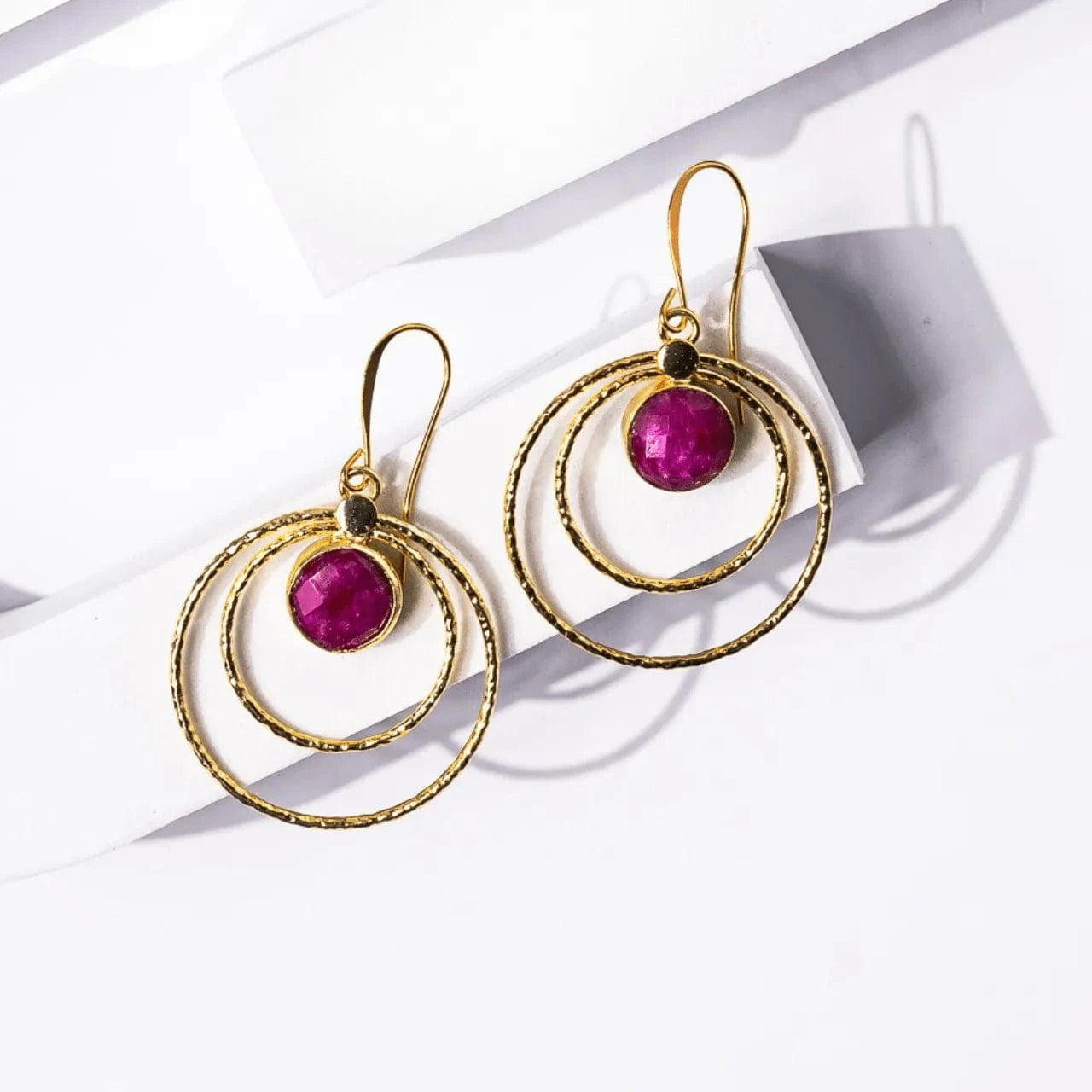 Gold earrings with pink gemstones on a white surface
