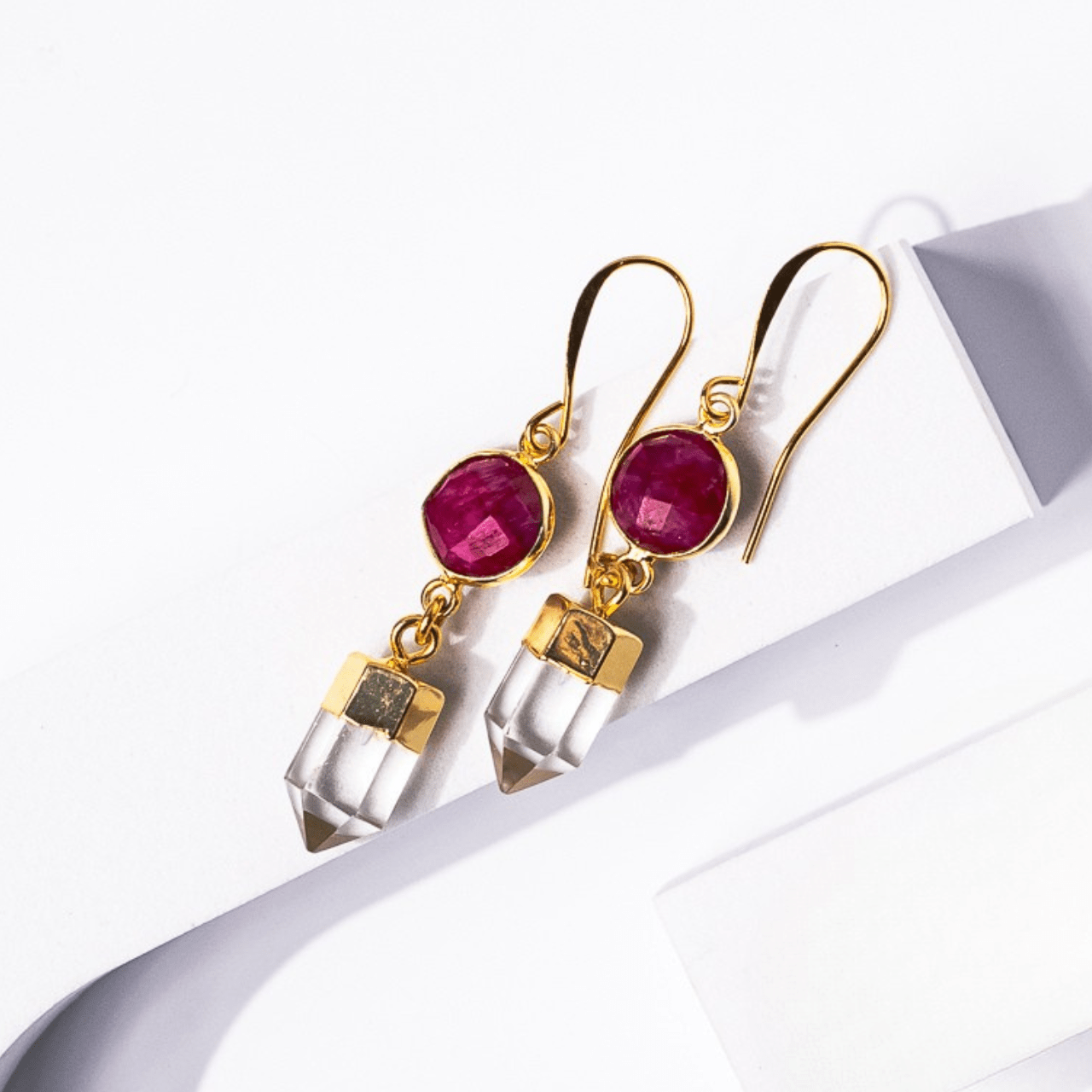 Gold earrings with red gemstones and clear crystal-like elements on a white background