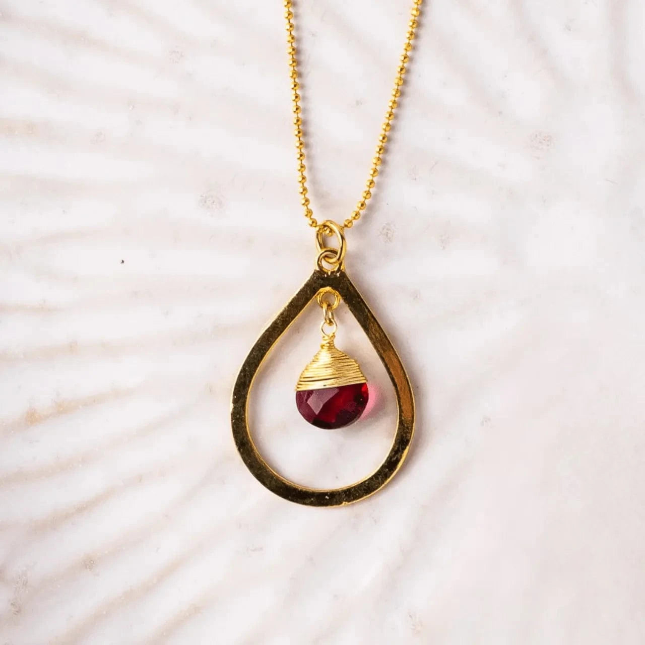 Necklace with a teardrop-shaped pendant featuring a red gemstone on a light background