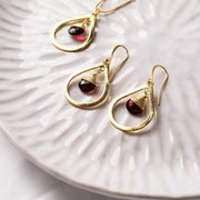 Gold earrings with red gemstones on a textured white plate