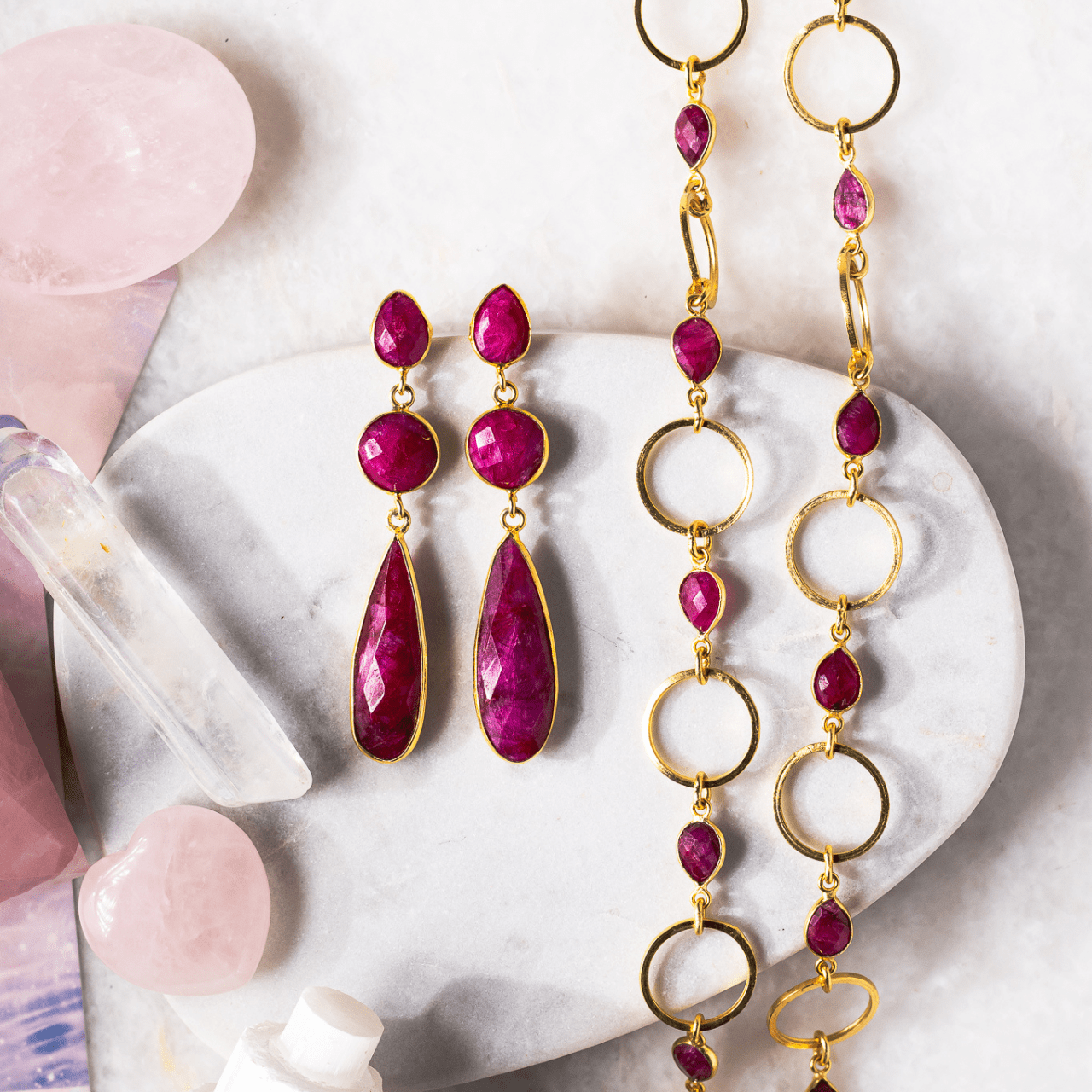 Gold and red gemstone earrings on a white stone surface with crystals.