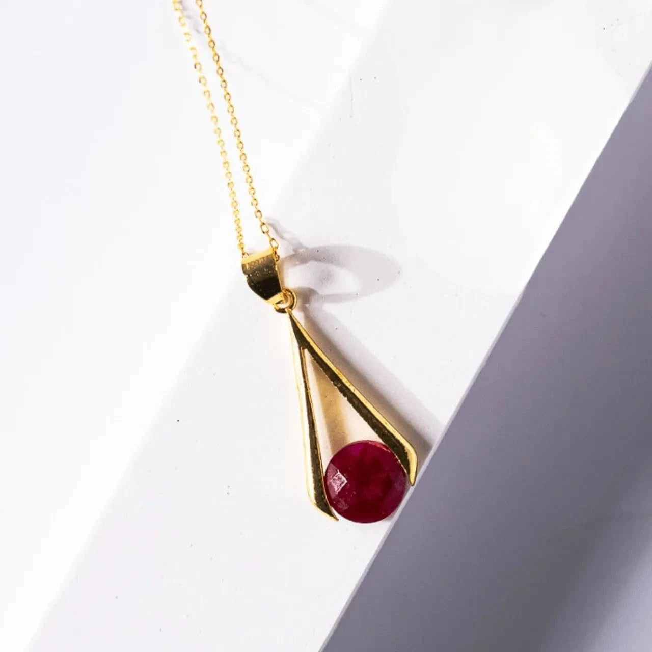 Gold necklace with a red gemstone pendant on a white background