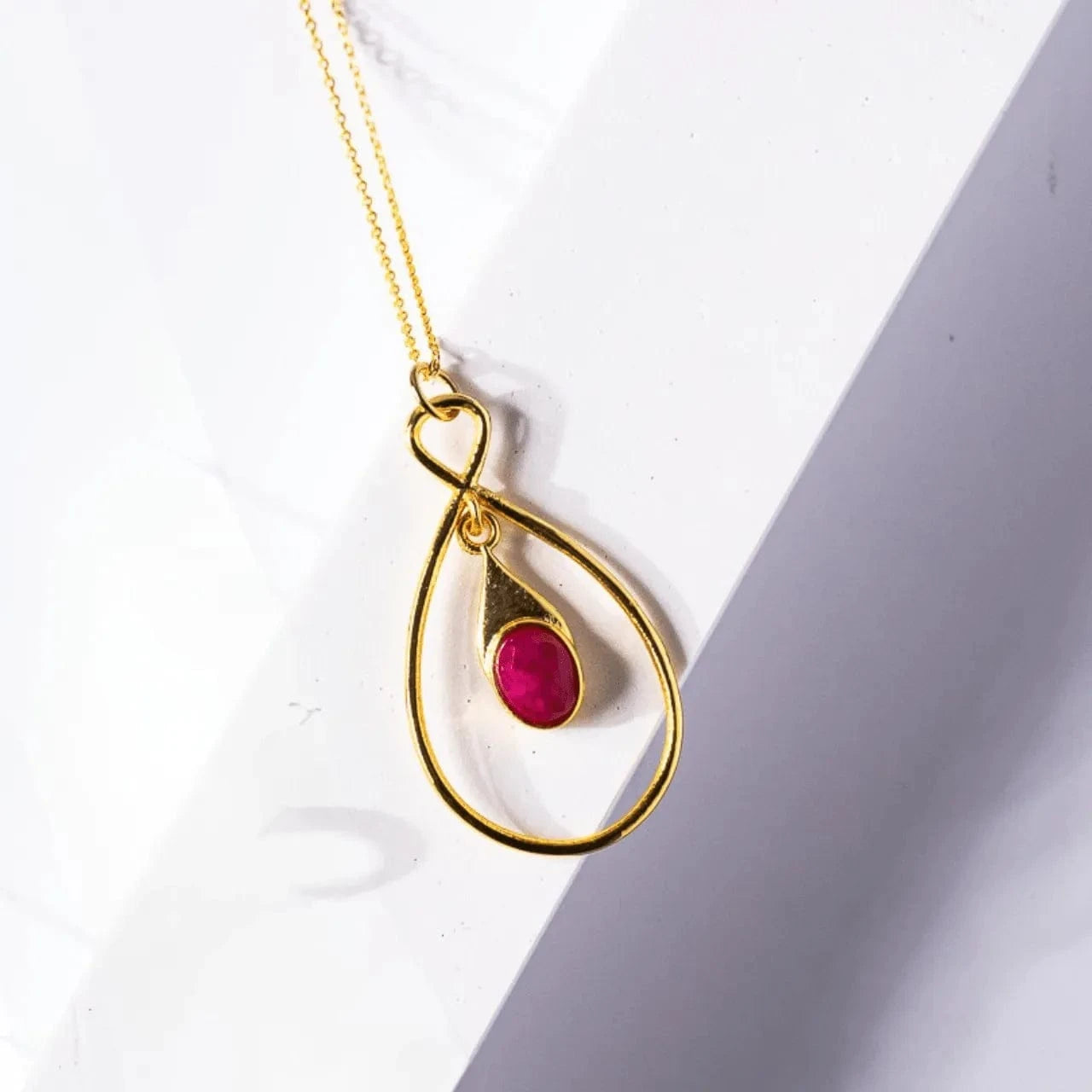 Gold necklace with a red gemstone pendant on a white background
