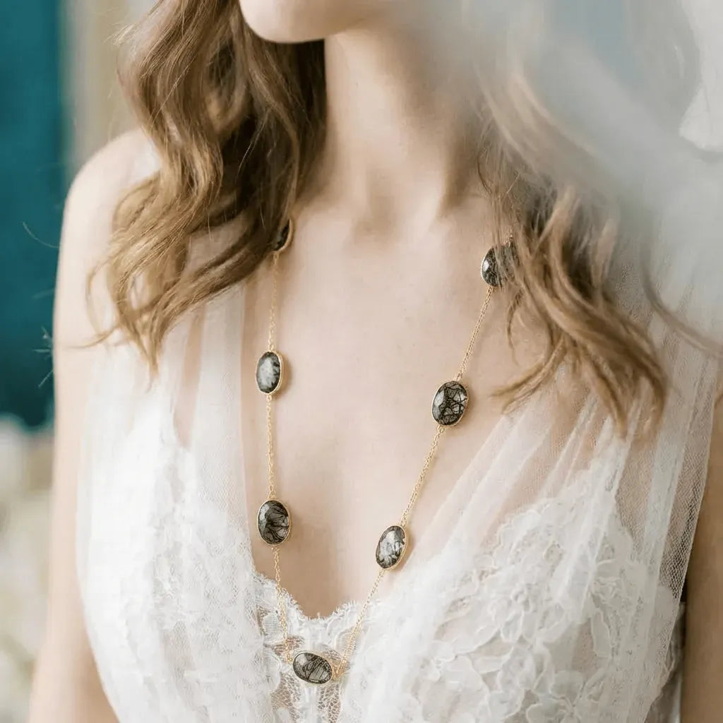 Close-up of a necklace with stones worn by a person in a lace garment.