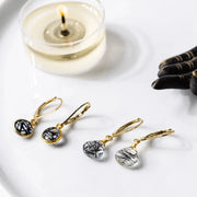 Gold earrings with black and green gemstones on a white surface next to a candle.