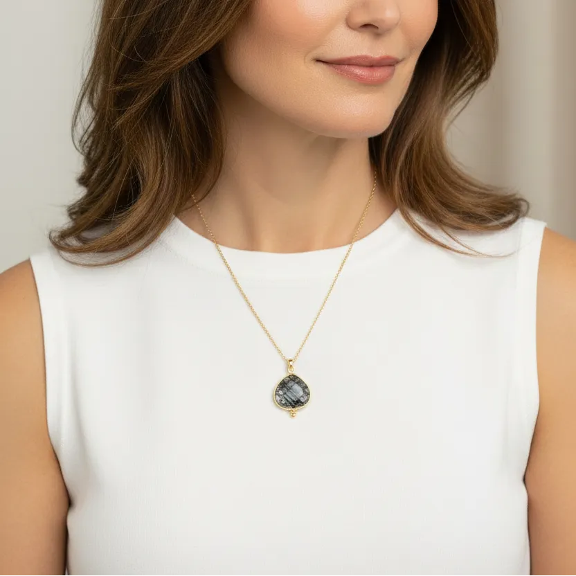 Woman wearing a gold necklace with a pendant against a neutral background