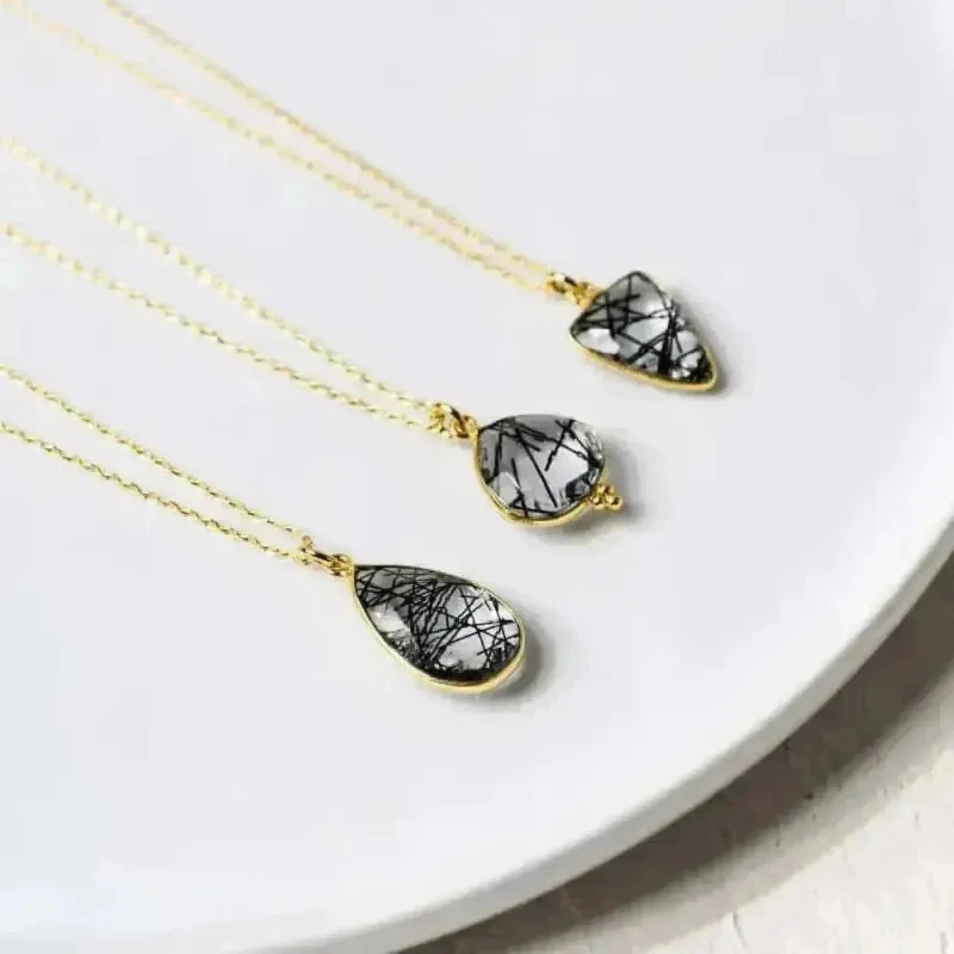 A collection of three rutilated quartz necklaces with teardrop designs, displayed on a white plate.