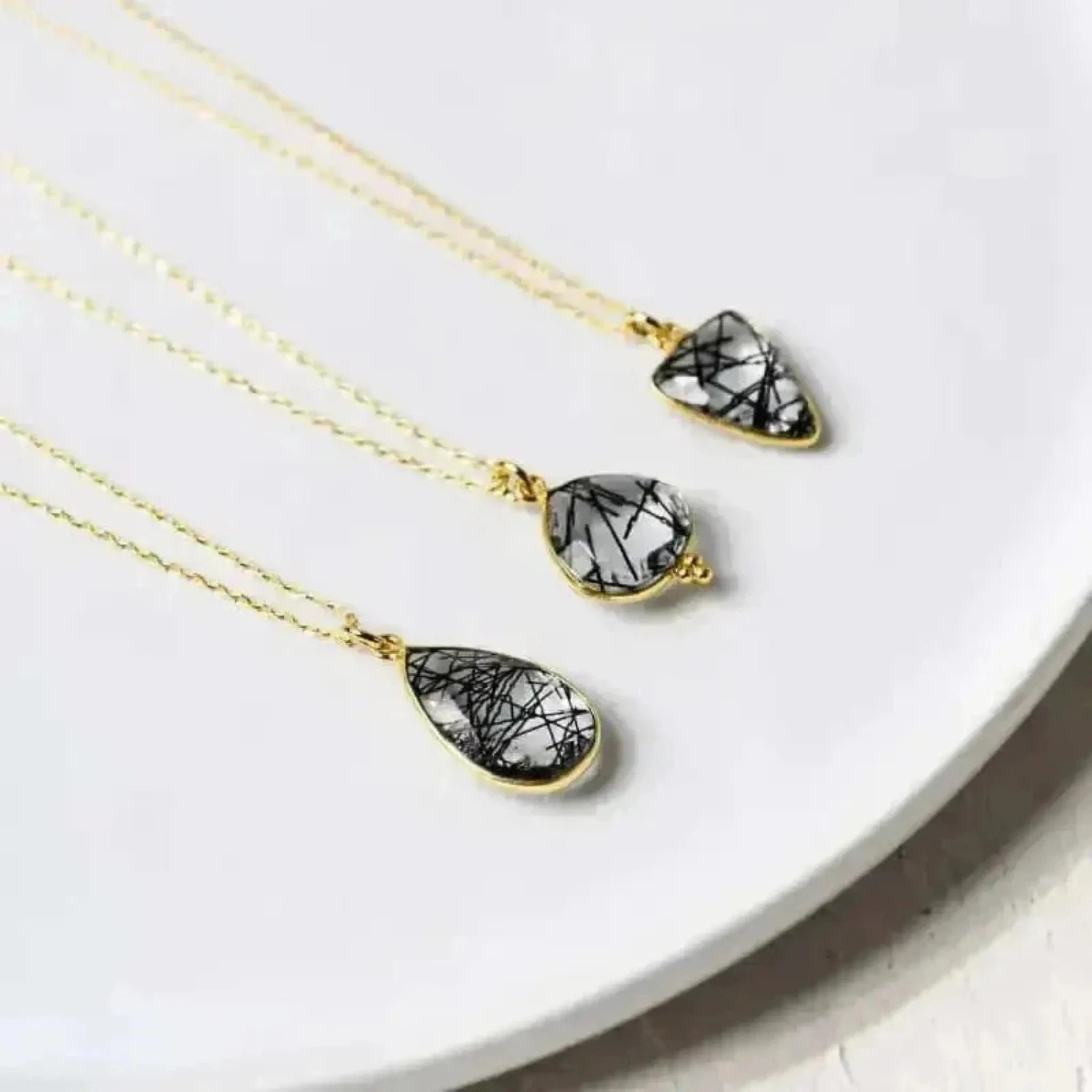 A collection of three rutilated quartz necklaces with teardrop designs, displayed on a white plate.