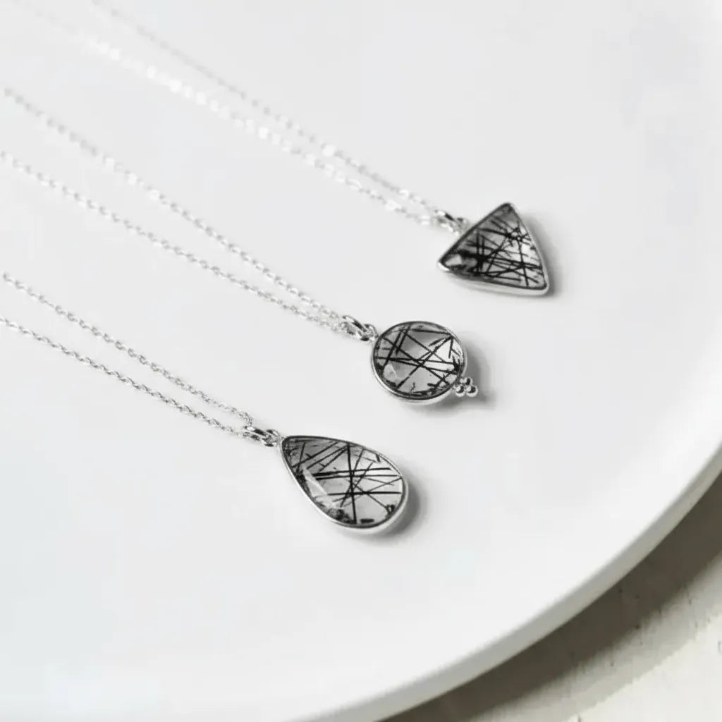 Two silver necklaces with geometric pendants on a white surface