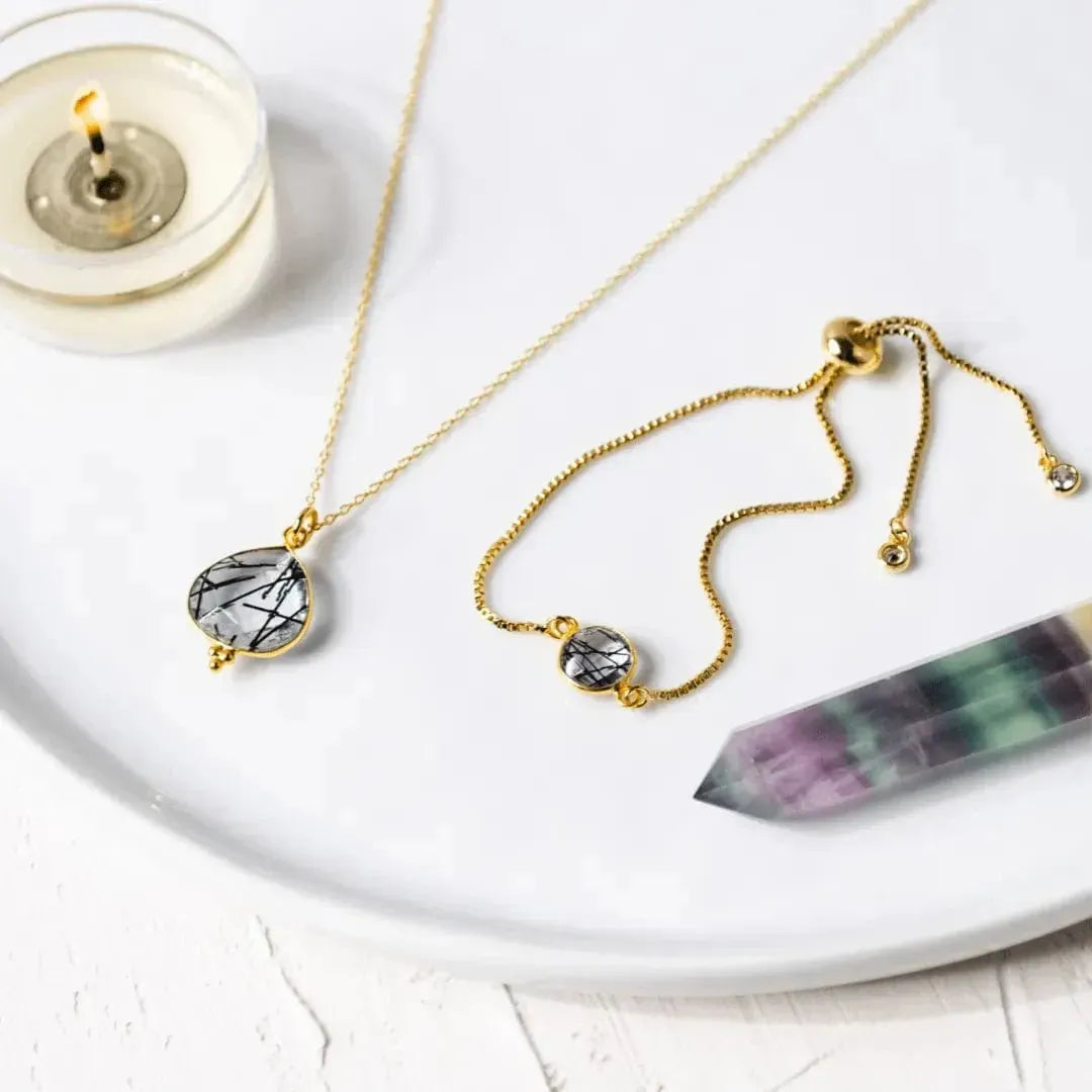 Gold necklace with a gemstone pendant on a white surface with a candle and crystal.