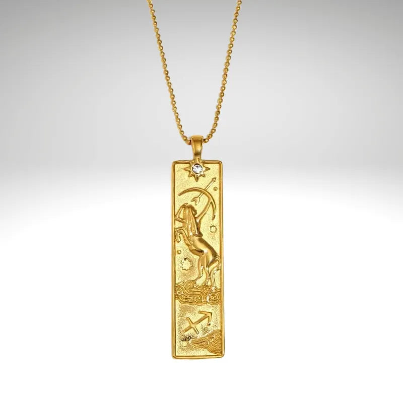Gold pendant with zodiac design on a chain against a light gray background