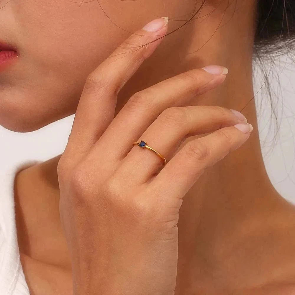 Close-up of a hand wearing a gold ring with a blue gemstone, touching the face.