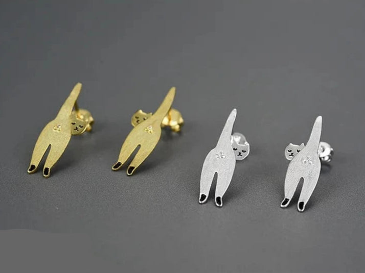 Cat-shaped stud earrings in gold and silver on a gray background