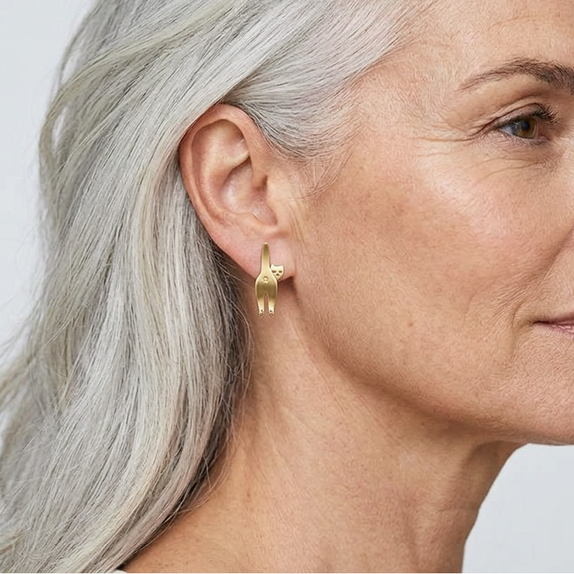 Gold cat-shaped earring worn by a person with long hair against a neutral background
