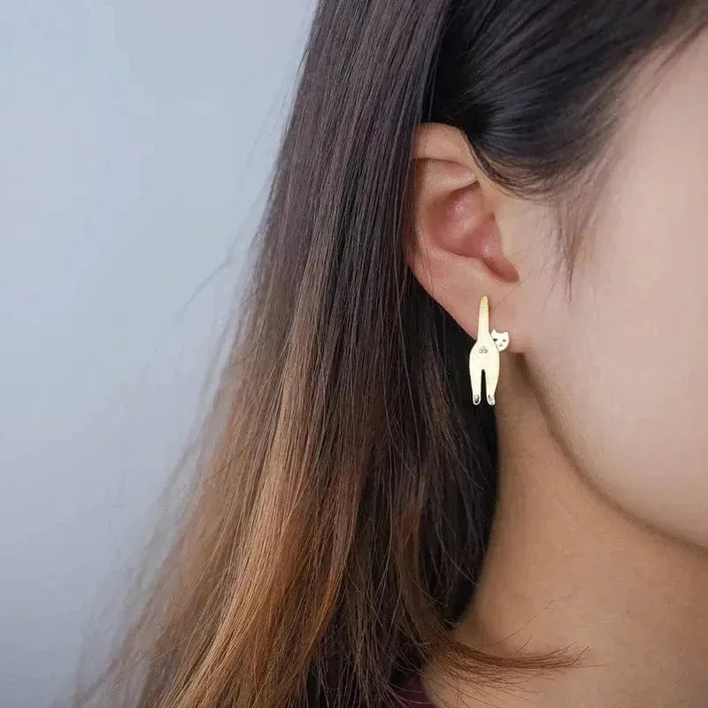 Gold cat-shaped earring worn by a person with long hair against a neutral background