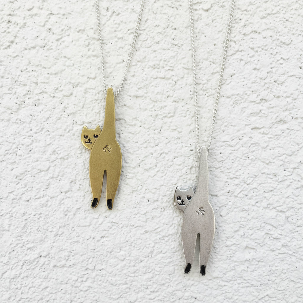 Two cat-shaped pendants, one gold and one silver, on a gray background.
