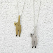 Two cat-shaped pendants, one gold and one silver, on a gray background.