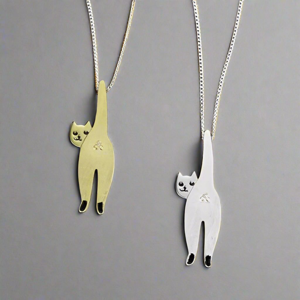 Two cat-shaped pendants, one gold and one silver, on a gray background.