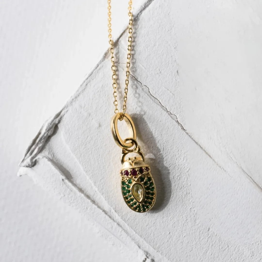 Gold necklace with a green and red pendant on a white marble surface